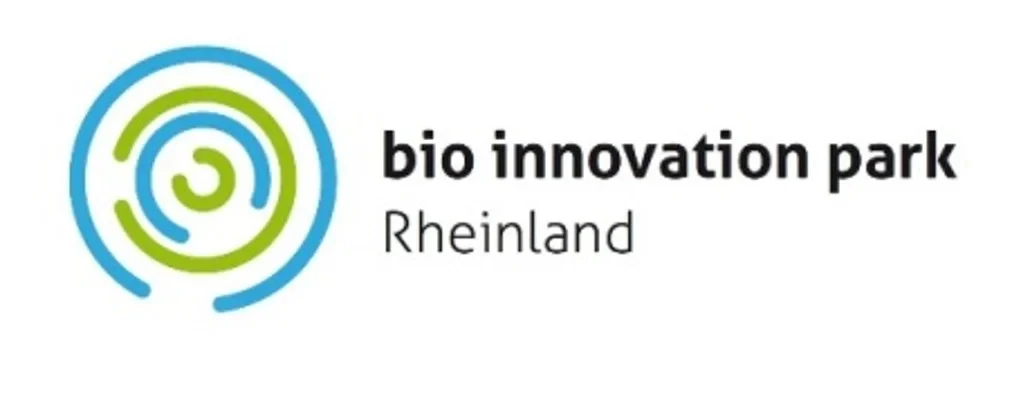 Eine Wissenschaftlerin und ein Wissenschaftler arbeiten hinter einer Glasfassade und mischen Chemikalien mit Großgeräten.